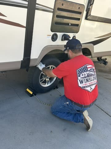 Technician servicing a travel trailer wheel with a chock in place