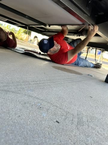 Technician lying under an RV reaching into the frame